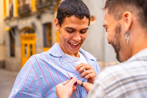 Gay man happily receiving a pride flag pin from his partner on a city street, joyful embrace and