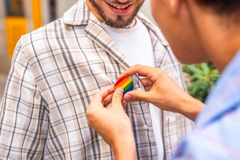 Gay partner pinning a rainbow pride badge to their partner's plaid shirt, close up of hands showing