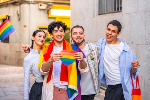 Diverse group of young adults smiling and celebrating pride in the city, holding a rainbow heart