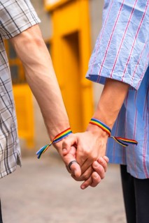 Male couple showing love and support for each other by holding hands with rainbow flag bracelets,