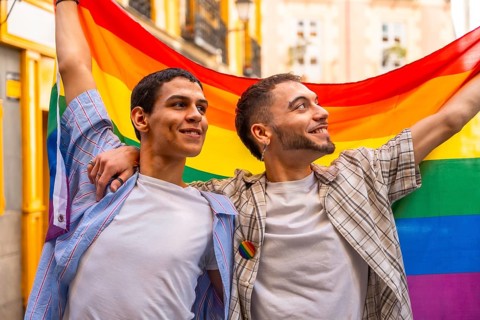 Two smiling men embracing and proudly displaying the vibrant rainbow flag, symbolizing lgbtq plus