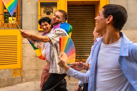Happy men are walking together on a street during a pride event, holding a small rainbow flag and a