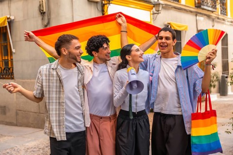 Diverse group of young adult friends smiling and holding a rainbow flag, fan, megaphone, and tote