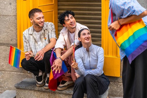 Group of diverse friends expressing joy and belonging, holding rainbow flags and carrying a rainbow