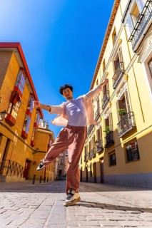 Young man actively posing and dancing on a cobblestone city street in historic european