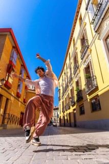 Man dancing energetically on a sunny cobblestone street in madrid, showcasing urban style and