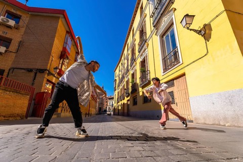 Two young male dancers performing contemporary street dance move on a sunny cobblestone street,