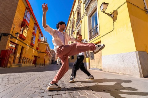 Two energetic young men are performing a dynamic dance routine on a cobblestone street, expressing
