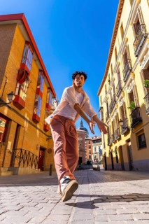 Young man striking a dynamic urban dance pose on sunlit cobblestones in madrid, radiating energy,