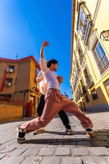Two young men engaging in an energetic dance performance on a sunny historic cobblestone street,