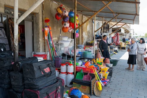 A shopping street with toys and household goods, meat hanging in front of the door, customers