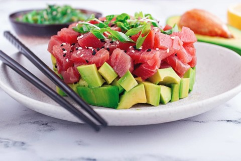 Fresh tuna tartare with avocado served on a marble table with soy sauce and seaweed salad