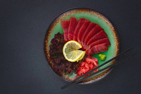 Fresh tuna sashimi served with lemon, wasabi, and pickled ginger on a dark background