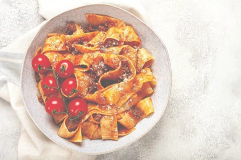 Pappardelle pasta with bolognese sauce, topped with parmesan cheese and cherry branch, homemade, no