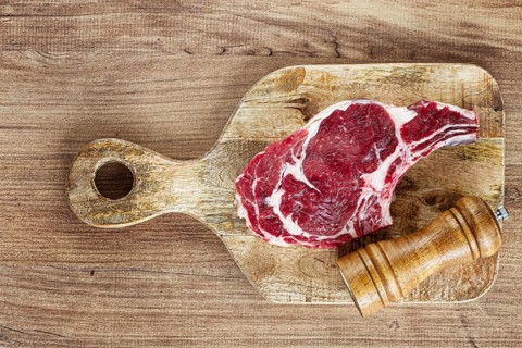 Raw rib eye steak, cowboy steak, on a wooden chopping board, top view, no people