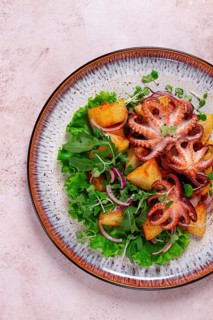 Grilled octopus with baked potatoes and fresh herbs, on a decorative plate, homemade