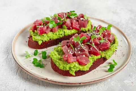 Toasts with fresh tuna and avocado, spread on black bread and sprinkled with microgreens,
