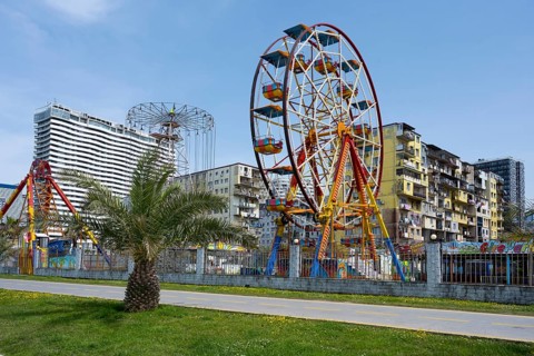 A colourful amusement park with a Ferris wheel against an urban backdrop under a clear sky,