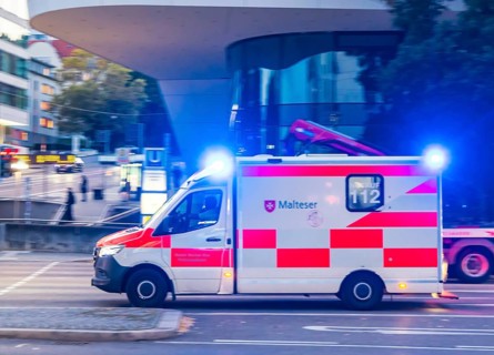 Ambulance of the BOS organisation Malteser with blue lights in an urban environment. Pulling along.