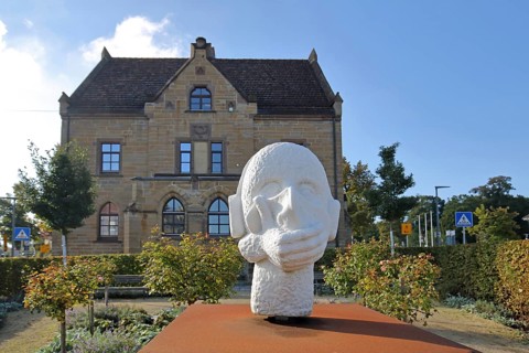 Sculpture head with headphones and hand for in front of the mouth, ambivalent symbolism for peace,