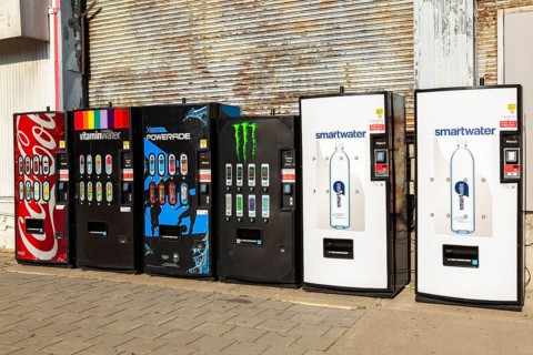 Row of popular bottled cold soft drinks and mineral water brands for sell in vending machines on