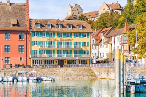Hotel building with colourful facades on the shore and docked boats in sunny weather, Meersburg,
