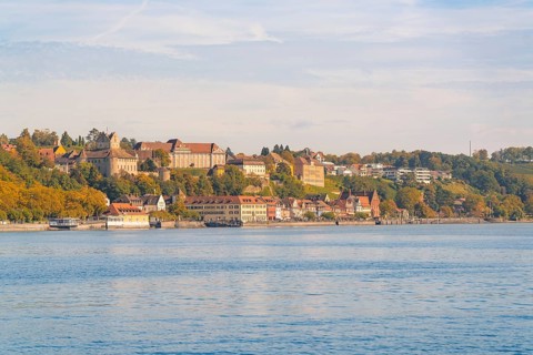 Town view on the lakeshore with historic buildings and autumnal trees under a blue sky, Meersburg,