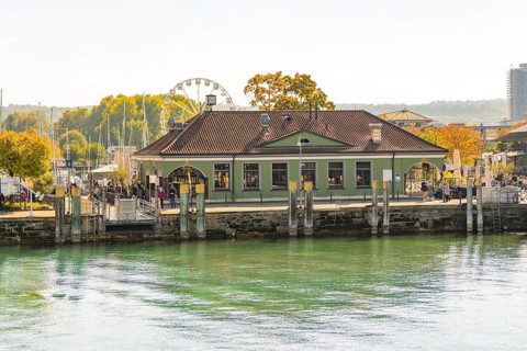 A building at the harbour with autumnal vegetation and a Ferris wheel in the background in a