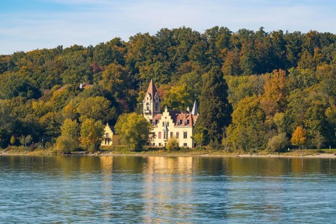 A picturesque castle on the shore of a lake surrounded by autumnal trees with a clear sky,