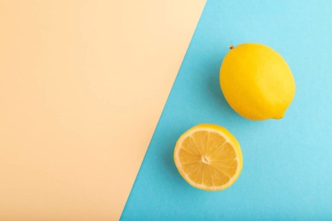Yellow Lemon Cut in half on orange and blue pastel paper background. Top view, flat lay, copy space