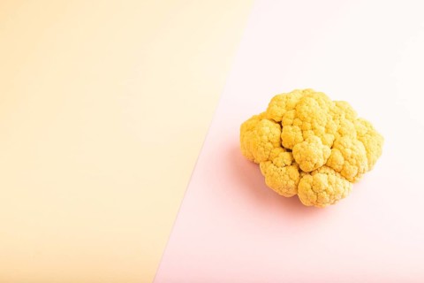 Yellow Cauliflower on pink and orange pastel paper background. Side view, copy space. healthy food,