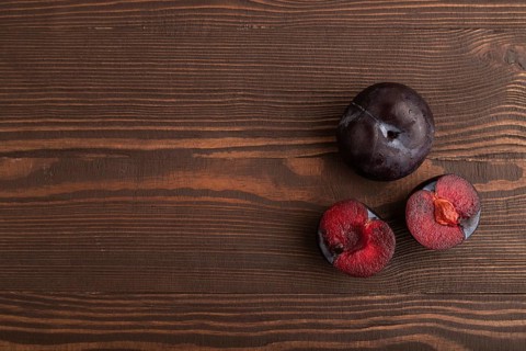Purple Plum Cut in half on brown wooden background. Top view, flat lay, copy space. healthy food,