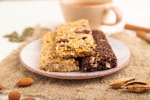 Granola bars with caramel, nuts, flakes in ceramic plate on white wooden background, beige linen