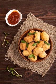 Fried crispy Chicken Nuggets with ketchup, microgreen on brown wooden background and linen textile.