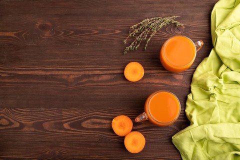 Two glasses with carrot juice, on wooden background and green textile. Diet, healthy eating concept