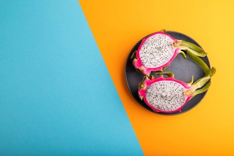 Ripe Pitaya on blue plate on blue and orange pastel paper background, top view, flat lay, copy