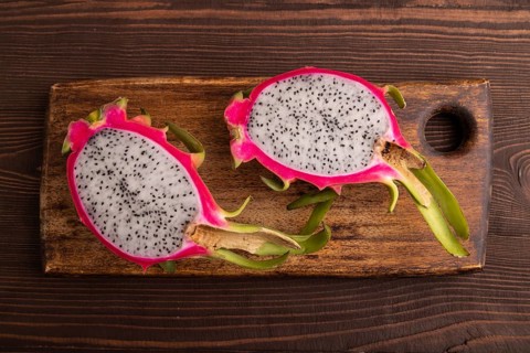 Ripe Pitaya on cutting board on brown wooden background, top view, flat lay, close up, minimalism