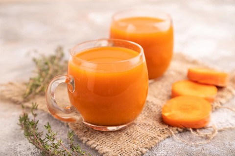 Two glasses with carrot juice, on brown concrete background and linen textile. Diet, healthy eating