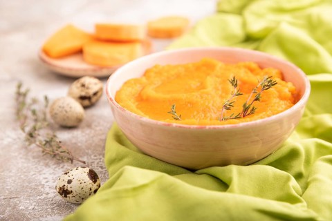 Sweet potato porridge in ceramic bowl on brown concrete background and green textile. Diet, healthy