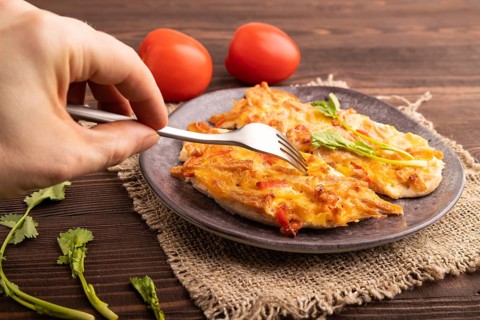 Baked chicken meat with cheese and tomatoes with hand on brown wooden background and linen textile.