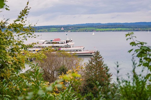 A large lake with a boat, surrounded by green landscape and cloudy sky, Mainau Island, Lake
