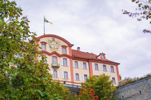 A magnificent building with a flag in the foreground, surrounded by autumnal greenery, Mainau