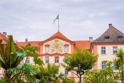 Historic building with a flag and plants in the garden, Mainau flower island, Lake Constance,