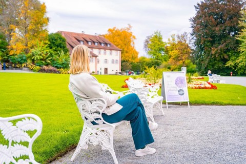 Woman sitting on a white garden bench, in the colourful autumn garden, Mainau flower island, Lake