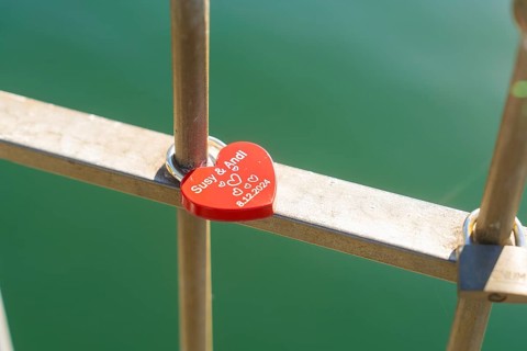 Red heart lock with engraving on the railing over green water, Überlingen, Lake Constance, Germany