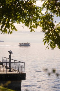 A boat passes by on a calm lake, visible from a binocular viewpoint next to a jetty, Überlingen,