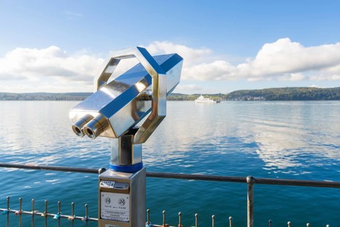 Metallic binoculars pointing to the lake with a peaceful view of the shore, Überlingen, Lake