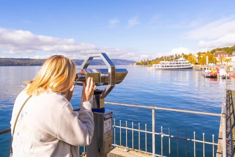 A woman looks through a telescope at a lake with ships and a clear autumn sky, Überlingen, Lake