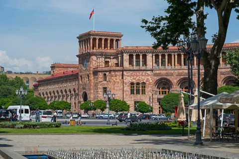 An impressive historic stone building with colonnades, surrounded by people and cars in an urban