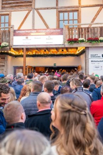 Crowds of people standing in front of the entrance to a wooden building, expectant atmosphere,